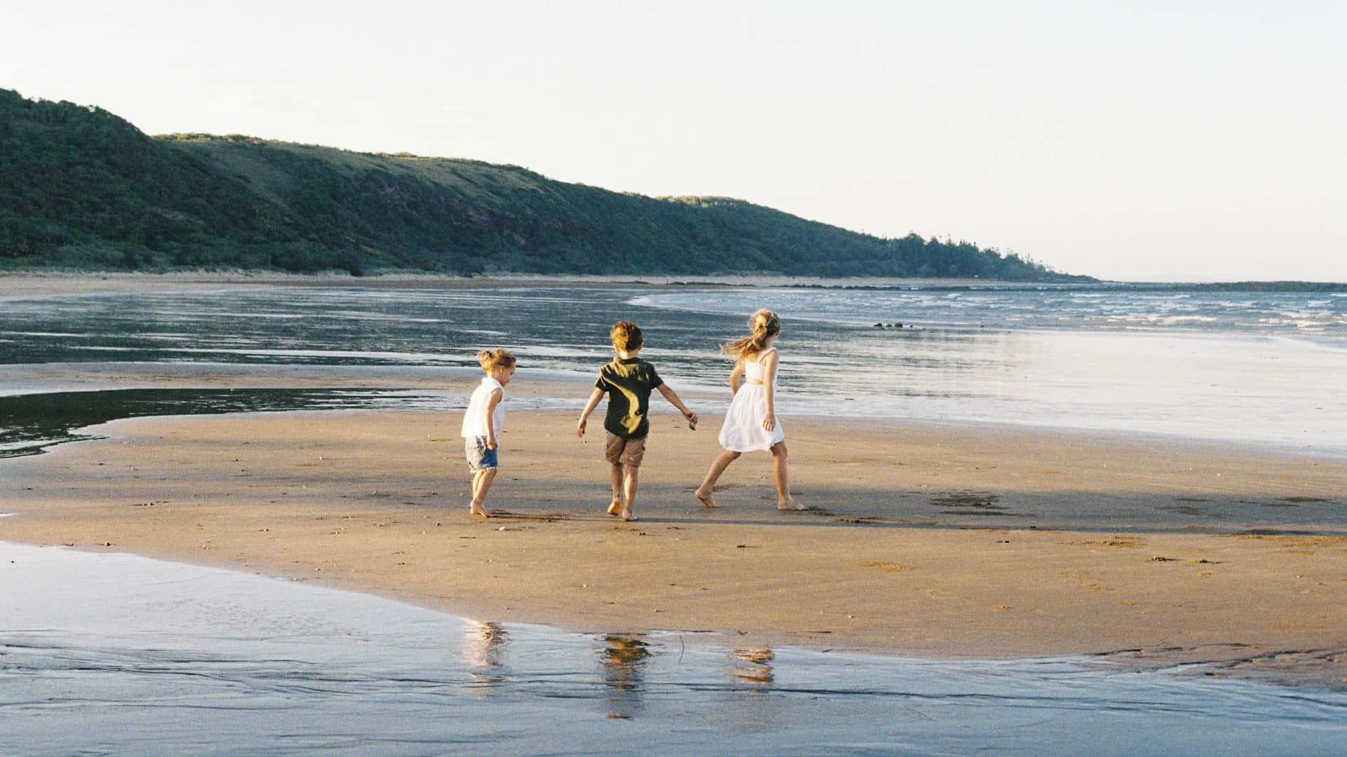 Children playing on a wide sandy beach in warm late afternoon light